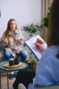 woman sitting on couch talking to her female therapist who is taking notes