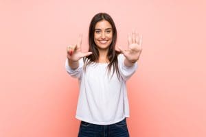 Myths about Addiction and Recovery, pretty young woman signing the number seven with her hands against a pink background - myths
