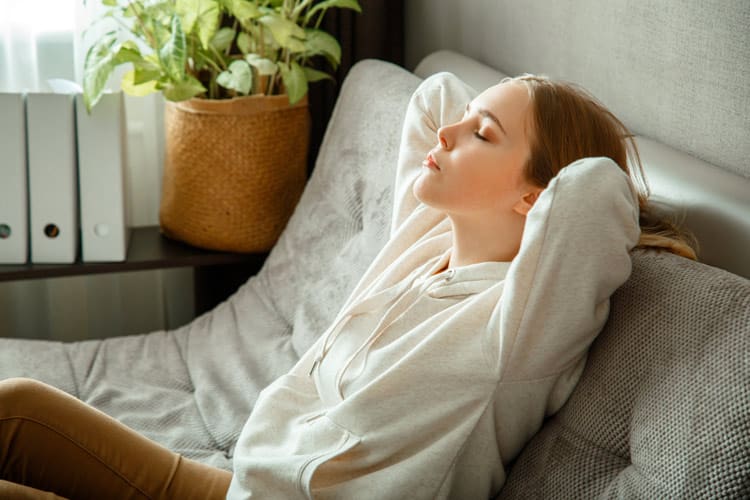 young woman relaxed and leaning back on couch with her eyes closed - mindfulness meditation