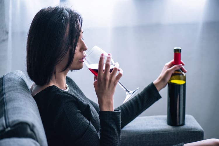 Withdrawal, pretty brunette woman drinking red wine at home - she has a glass and is holding the bottle - alcohol withdrawal