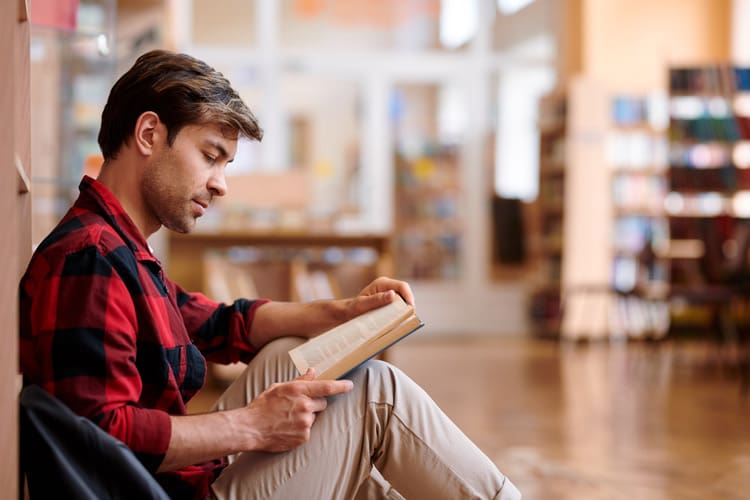 middle age man sitting in bookstore or library reading a book - addiction recovery