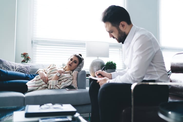 pretty young woman lying on couch in therapy session with attractive man - Cognitive-Behavioral Therapy