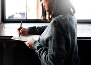 Recovery Journal, pretty woman sitting and writing in a journal near a brightly lit window - journaling