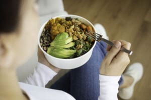woman eating a bowl of nutritious food - avocado, cauliflower, arugula and more