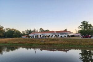 Anabranch Recovery Center, A single-story building with a red roof and white exterior, set against a backdrop of trees and reflected in a nearby pond