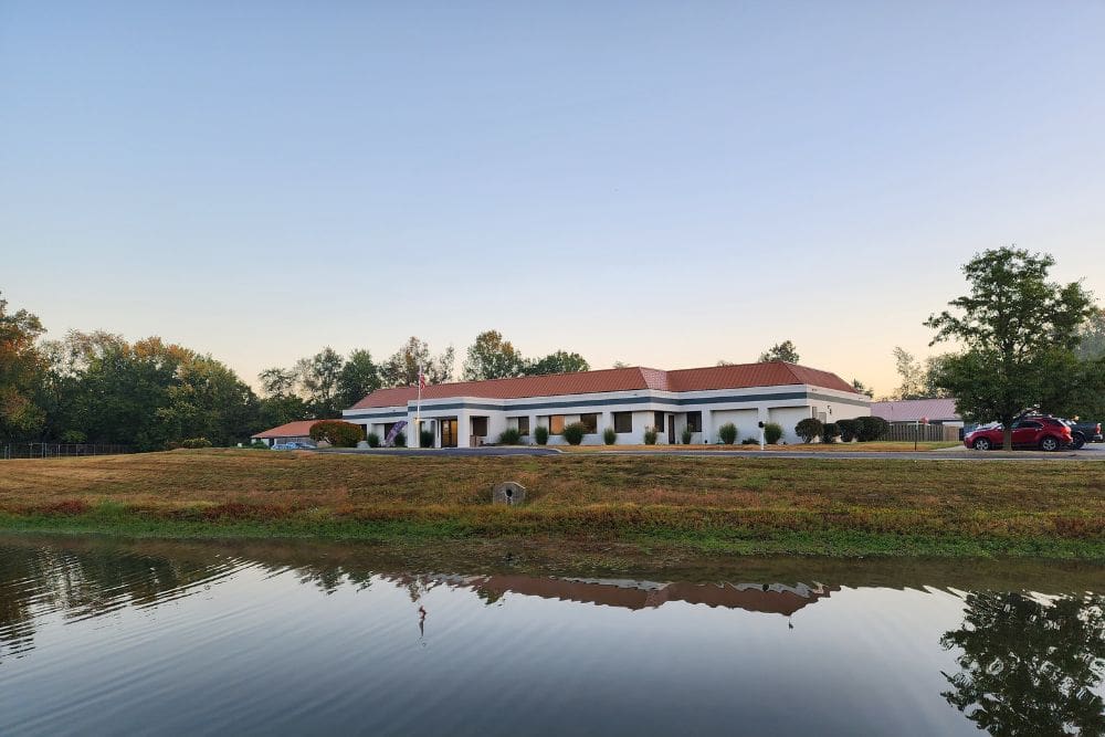 Anabranch Recovery Center, A single-story building with a red roof and white exterior, set against a backdrop of trees and reflected in a nearby pond