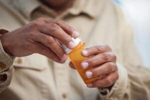 Close-up of a person in a beige shirt opening an orange prescription pill bottle