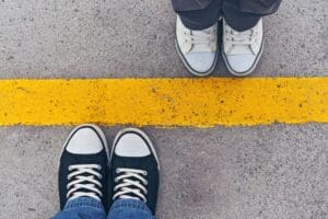 Two pairs of sneakers face each other on a concrete surface, separated by a bold yellow line, symbolizing personal boundaries.