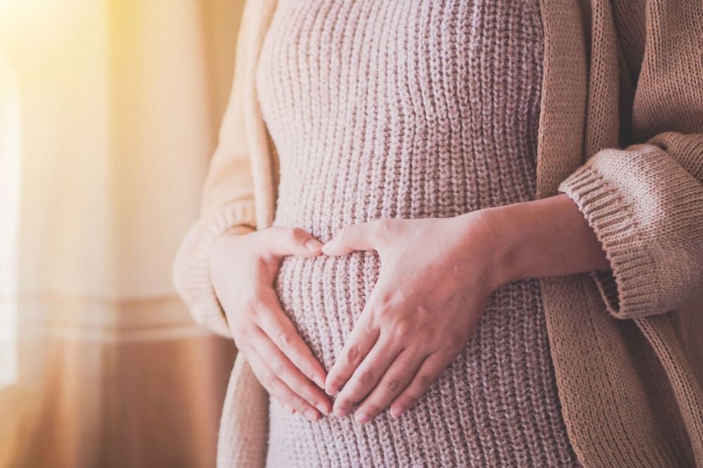 portrait of a pregnant woman with her hands on her belly in the shape of a heart.