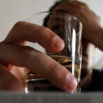 Alcohol blackout (1000 x 667 px) A person holds a glass of alcohol while resting their head in their hand, symbolizing struggle, dependence, or emotional distress related to drinking.