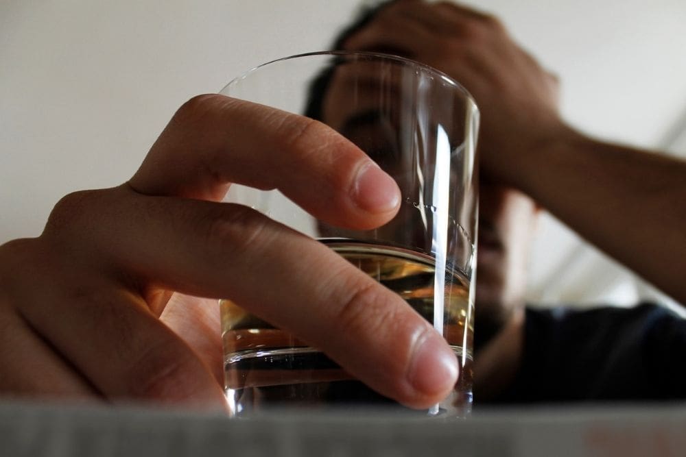 A person holds a glass of alcohol while resting their head in their hand, symbolizing struggle, dependence, or emotional distress related to drinking.