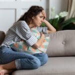 Anxiety and Panic disorder (1000 x 667 px) Woman sitting on a couch hugging a pillow, looking worried and deep in thought, suggesting anxiety or emotional stress.