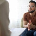 Therapy (1000 x 667 px) Man sitting and talking with a therapist during a counseling session, appearing thoughtful and engaged in conversation.