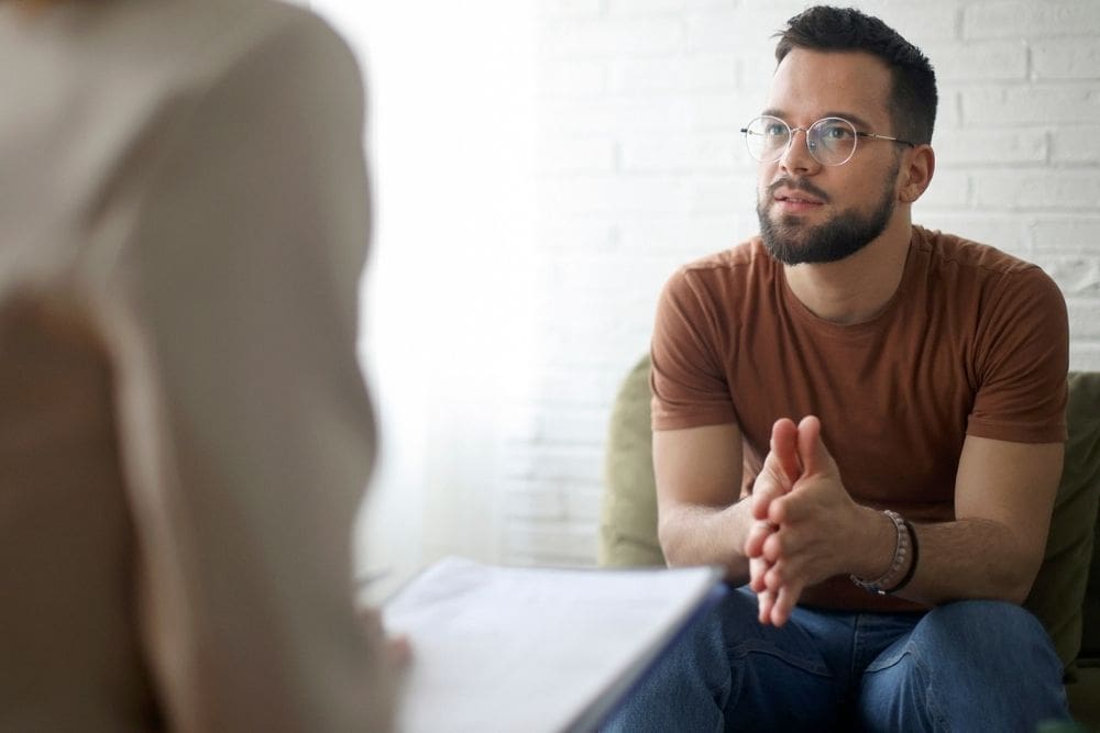 Man sitting and talking with a therapist during a counseling session, appearing thoughtful and engaged in conversation.