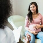 Pregnant person sitting with a healthcare provider during an appointment, discussing care and support in a clinical setting.