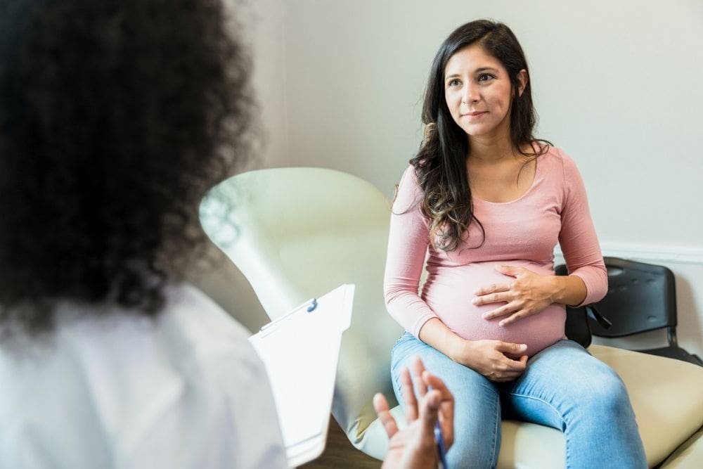Pregnant person sitting with a healthcare provider during an appointment, discussing care and support in a clinical setting.