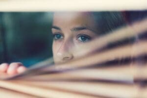 Anabranch - The Devastating Effects of Meth Use. A woman peers out of a window pulling the blinds down.
