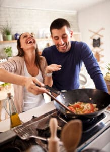 photo of a couple in the kitchen laughing and enjoying cooking food in a wok